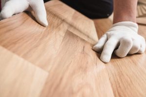 Hands pressing on an uneven flooring surface showing dips and lack of subfloor flatness.