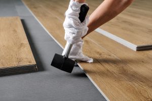 Installer tapping vinyl plank flooring into place over underlayment during a floating floor installation.