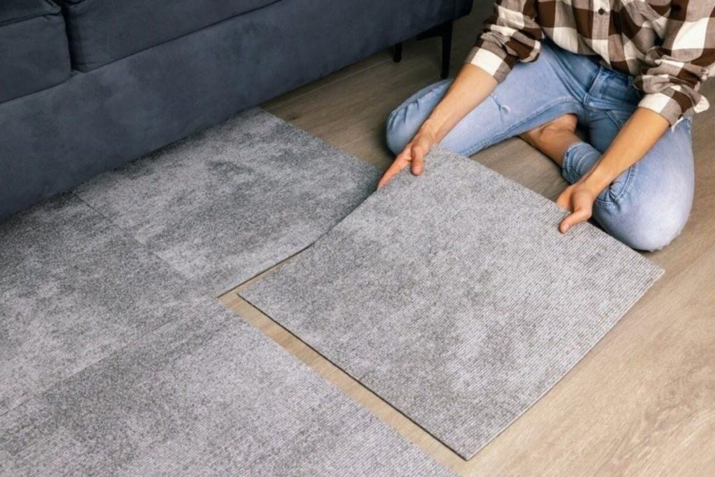 Person placing a grey carpet sample over existing condo flooring while checking floor height, transitions, and replacement planning in a Vancouver condo.